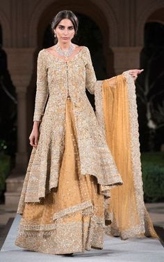 a model walks down the runway in a gold gown with an elaborate cape on top