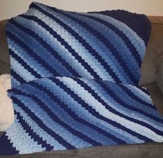 a blue and white blanket sitting on top of a couch next to a teddy bear