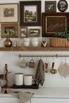 there are many pictures on the wall above the kitchen counter and below it is a shelf with pots, pans, utensils and other items