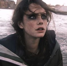 a woman with her hair blowing in the wind on top of a boat near water