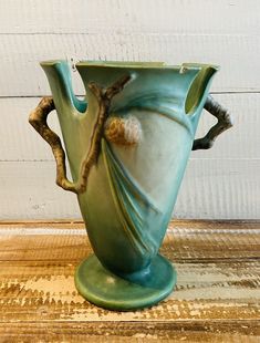 a green vase sitting on top of a wooden table next to a white painted wall