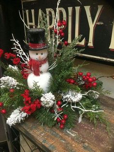 a snowman sitting on top of a wooden table covered in greenery and red berries