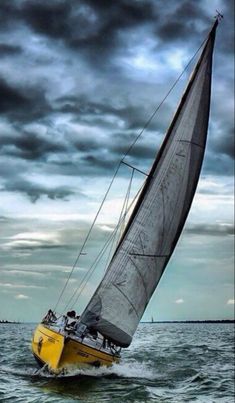 a yellow sailboat in the middle of the ocean under a cloudy sky with dark clouds