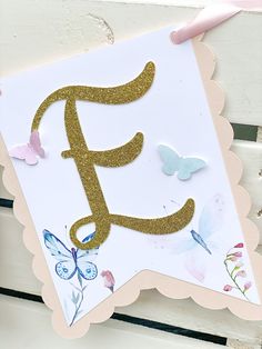 a card with the letter f in gold glitter and butterflies on it, sitting on a white bench