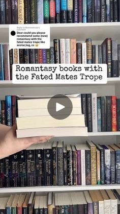 a person holding a stack of books in front of a book shelf filled with books