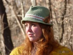 a woman with red hair wearing a green hat and looking off to the side in front of trees