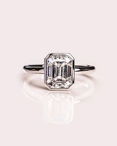 an emerald cut diamond ring on a white surface