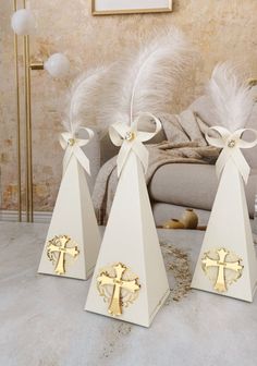 three white candlesticks with gold crosses and bows on them sitting in front of a couch