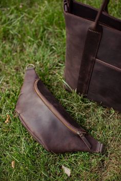 a brown leather bag sitting on top of a green grass covered field next to a purse