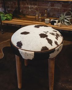 a cow print stool sitting on top of a brown floor next to a brick wall