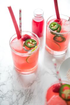 three glasses filled with drinks sitting on top of a marble counter next to two spoons