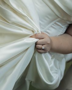 a woman in a white dress is holding on to her wedding ring as she hides behind the fabric