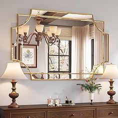 a large mirror hanging on the wall above a dresser with two lamps next to it