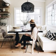 a woman sitting at a table in front of a window with a laptop on it