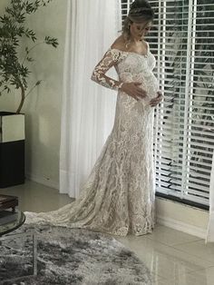 a pregnant woman in a wedding dress standing next to a window