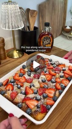 someone is cutting strawberries and blueberries into a dessert