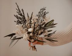 a person holding a bouquet of flowers in their hand with white and green leaves on it