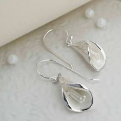 Delicate and stunningly simple these sterling silver calla lily earrings are flawless, combining the sophistication of silver with the beauty of nature. Adorn yourself with these everyday essentials. With an icing sugar finish, matte outer flute and polished lip to highlight the delicately detailed design. Whether its a little treat for yourself or that stylish someone special, these sterling silver calla lily earrings will add that fashion forward finishing touch to any outfit. All Martha Jackson jewellery comes complete with a gift box and blank gift card for you to write a message on Calla Lily Jewelry, Torch Fired Enamel Jewelry, Lily Jewelry, Lily Earrings, Bridesmaid Presents, Dangly Earrings, Matching Necklaces, Calla Lily, Shop Clothing