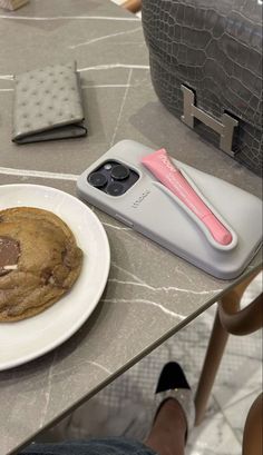 a chocolate chip cookie sitting on top of a white plate next to a cell phone