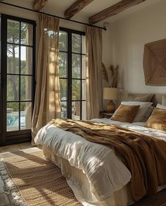 a large bed sitting next to a window in a bedroom under a wooden beam with curtains