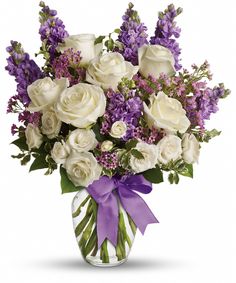 a bouquet of white roses and lavenders in a glass vase with purple ribbon on the side