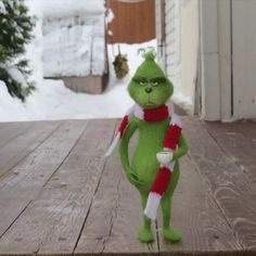 a green stuffed animal with a red and white scarf on it's neck holding a cup