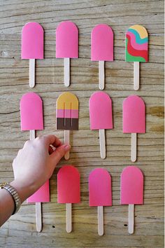 popsicles made out of paper are being held by a person's hand on a wooden table