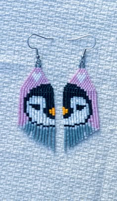 a pair of beaded penguin earrings hanging from a hook on top of a blue shirt