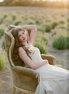 a woman in a white dress is sitting on a chair with her arms behind her head