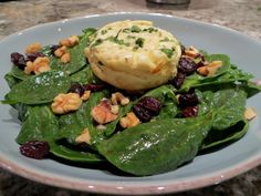 a plate with spinach, cheese and nuts on it sitting on a marble table