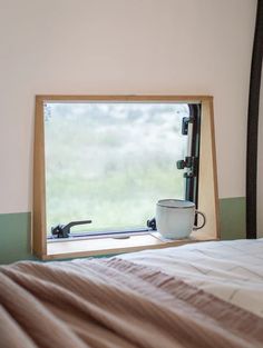 there is a coffee cup sitting on the edge of a window sill next to a bed