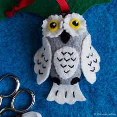 an owl ornament sitting next to scissors on a blue surface with a red ribbon