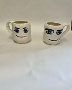 two mugs with faces painted on them sitting next to each other in front of a white background