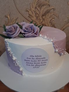 a white cake with purple frosting and flowers on top, sitting on a table