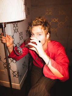 a man sitting on the floor drinking from a wine glass in front of a lamp