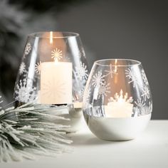 two candles are sitting on a table next to some snowflakes and pine cones