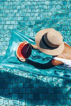 a woman in a hat sitting on the edge of a swimming pool with a drink