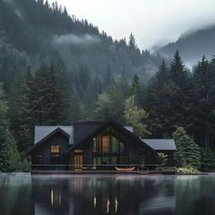 a house sitting on the edge of a lake surrounded by trees and foggy mountains