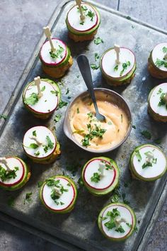 small appetizers are arranged on a tray with a spoon in one bowl and garnishes in the other