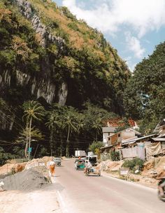 a man riding a motorcycle down a street next to tall mountains and palm trees in the background