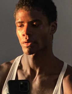 a young man taking a selfie with his cell phone in front of him while wearing a white tank top