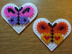 two heart shaped magnets made out of beads on top of a wooden table next to each other