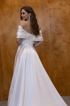 a woman in a white wedding dress standing next to a wood paneled wall and looking off into the distance