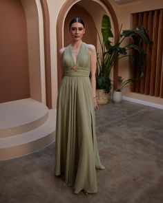 a woman in a long dress standing next to a potted plant and indoor area