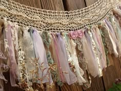 an old lace banner with flowers and ribbons hanging from it's sides on a wooden fence