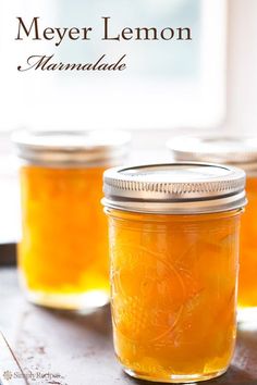 three mason jars filled with lemon marmalade sitting on a wooden table next to a window