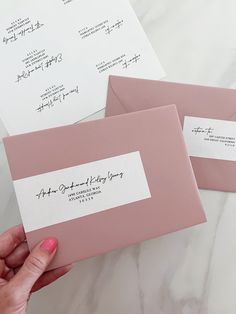 two pink envelopes with handwritten labels on them are being held by a woman's hand