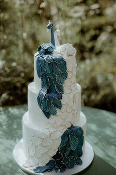 a three tiered cake with blue and white decorations on the top is sitting on a green table