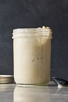 a jar filled with white liquid sitting on top of a table next to a spoon