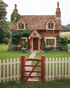 a red gate in front of a house with a white picket fence and green grass